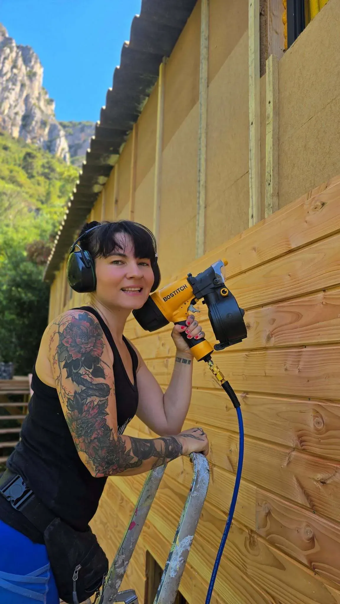 Diane pose le bardage de la cabane, pistolet à peinture en main